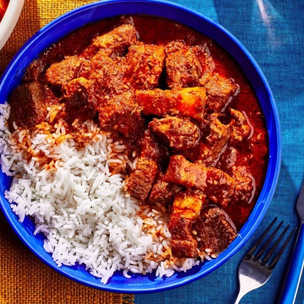 Indian lamb curry with white rice in a blue bowl on a blue and orange tablecloth.