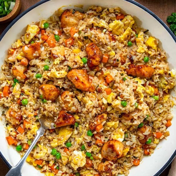 Chicken fried rice with peas, carrots, and scrambled egg in a white pan with a spoon.