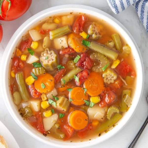 A vibrant bowl of Indian vegetable soup with carrots, okra, tomatoes, corn, and potatoes.