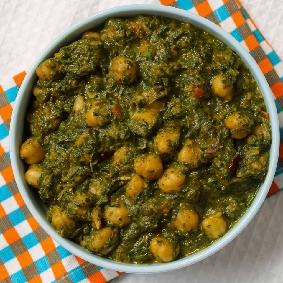 A light blue bowl filled with green Indian saag chana, a spinach and chickpea curry, on a checkered napkin.